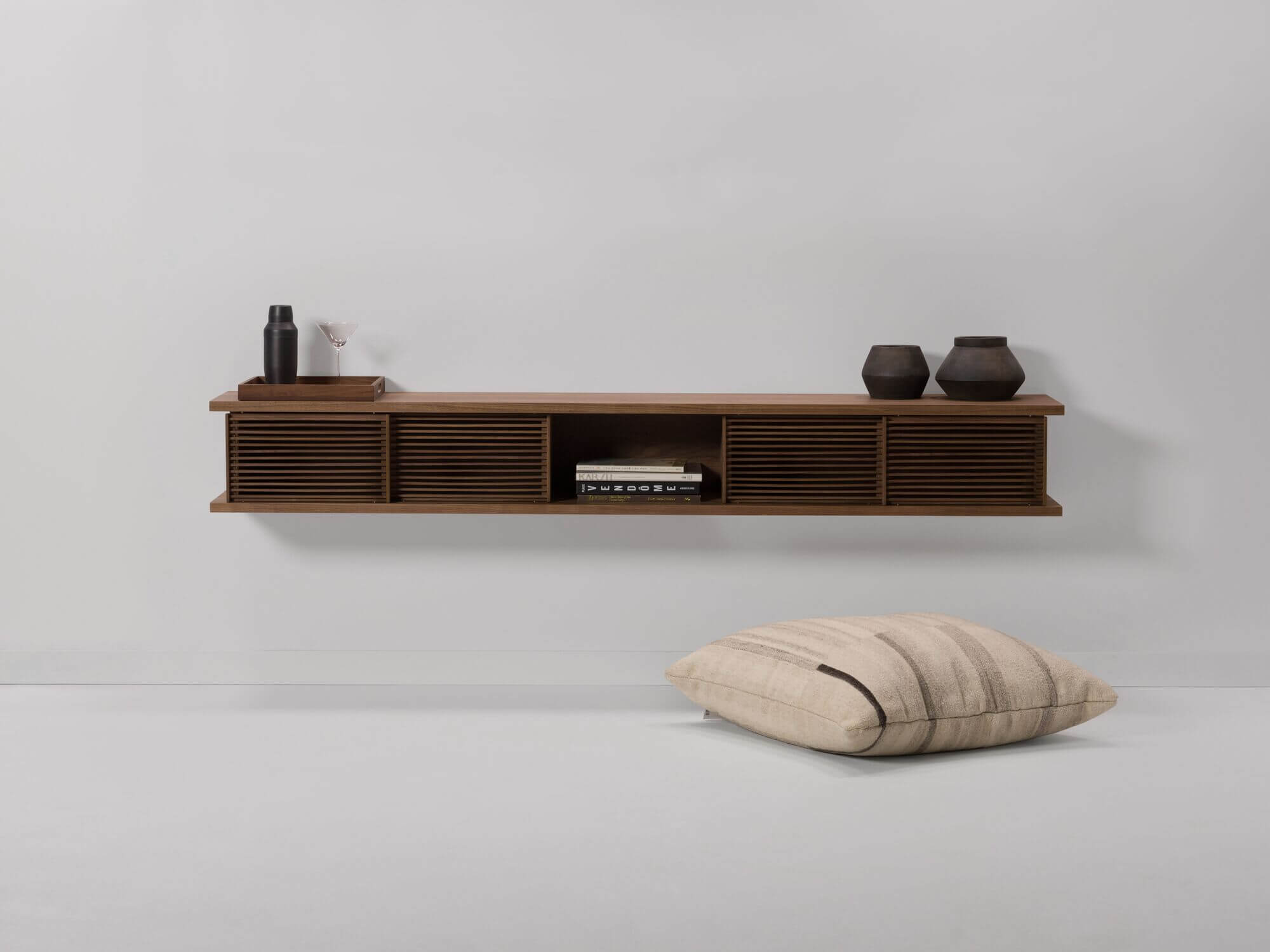 Large walnut floating wall shelf with floor pillow beside it and vases on it